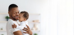 Child Care. Portrait Of Happy African American Father With Infant Baby In Arms Standing Near Window At Home, Young Black Dad Spending Time With Adorable Toddler Child, Panorama With Copy Space