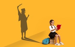 Cheerful Asian Schoolgirl Reading, Sitting On Book Stack, Shape Of Female In Graduation Costume Over Yellow Background, Kid Dreaming About Master Degree, Conceptual Image, Panorama
