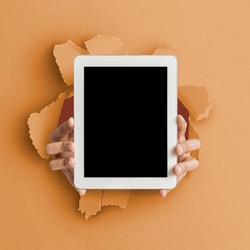 App Advert, Great Offer. Closeup of person holding tab with empty screen in hands showing device close to camera breaking through orange paper sheet hole. Gadget display with free copy space, mock up