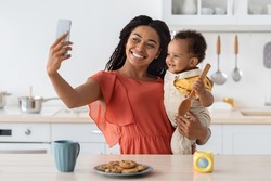 African American Mother Taking Selfie With Her Little Baby On Smartphone In Kitchen Interior, Happy Black Woman Making Photos With Cute Infant Child At Home, Enjoying Spending Time Together