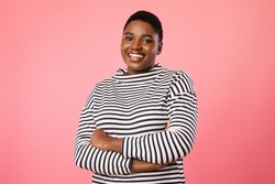 Pretty Overweight African American Woman With Short Haircut Posing Wearing Striped Longsleeve Smiling To Camera Standing Over Pink Background. Studio Shot
