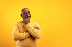 Thoughtful senior African American man looking aside at empty space, touching his chin, deep in thought on orange studio background. Dreamy elderly black male offering place for your advertisement