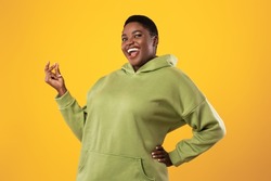 Joyful Overweight Black Woman Snapping Fingers Smiling To Camera Standing Posing Over Yellow Studio Background. It's Easy, Finger Clicking Gesture Concept