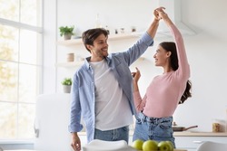 Happy cheerful attractive young husband and wife dancing and have fun together in kitchen interior, empty space. Couple enjoy domestic romantic date in own new home together on weekend and free time