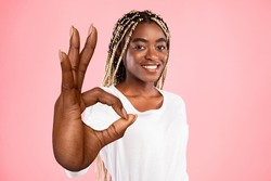 Beautiful young black woman showing big OKAY gesture on pink studio background. Lovely African American female expressing her approval or support, giving positive feedback