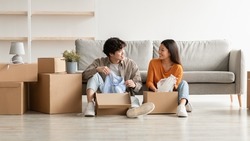 Relocation day concept. Cheerful millennial Asian couple unpacking belongings and having conversation, moving to new apartment or their own house, copy space. Panorama