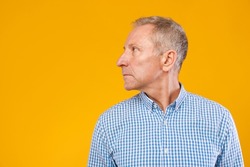 Profile portrait of serious pensive mature man looking aside at free copy space. Headshot of confident half turned male adult posing standing isolated on yellow orange studio background wall