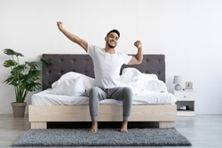 Handsome Happy Young Arab Guy Waking Up In The Morning, Sitting On Bed And Stretching After Good Sleep, Smiling Millennial Middle Eastern Man Having Good Mood, Enjoying Start Of New Day, Copy Space