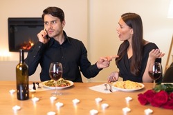 Relationship Conflicts Concept. Annoyed angry woman looking and yelling at her man who talking on cellphone and showing her finger to shut up and to wait while having date in restaurant