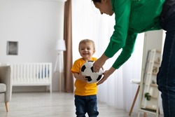 Happy caucasian mother and her toddler son playing with soccer ball at home, having fun and enjoying time together, free space. Maternity leave, childhood and leisure time concept