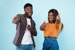 Hey, You. Portrait of cheerful African American guy and lady pointing two index fingers at camera, standing isolated over blue studio background wall. Positive young friends choosing and indicating