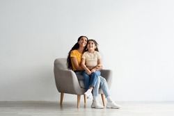 Look There. Amazed Mom And Her Little Daughter Sitting In Armchair And Looking Up Above Their Heads With Excitement, Interested Middle Eastern Mother And Female Kid Emotionally Reacting To Offer