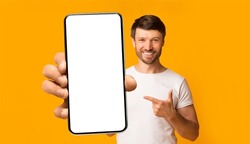 Recommendation. Portrait of excited bearded man holding big smartphone with white blank screen in hand, showing close to camera and pointing at device. Gadget with empty free space for mock up, banner