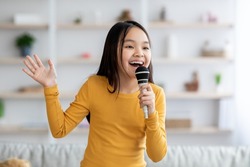 Portrait of cute pretty long-haired korean girl teenager singing at home, using microphone and gesturing, looking at copy space. Child singing karaoke, domestic entertainment for kids concept