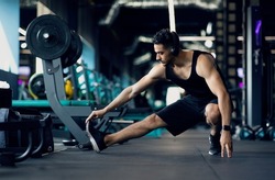 Handsome Young Middle Eastern Male Athlete Warming Up Before Training At Gym, Motivated Millennial Arab Man Stretching Leg Muscles, Preparing For Fitness Workout In modern Sport Club, Copy Space