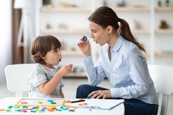 Female speech therapist curing child's problems and impediments. Little boy learning letter O with private English language tutor during lesson at office
