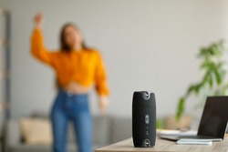 Young lady dancing to popular music at home, selective focus on portable wireless speaker, copy space. Millennial woman enjoying dance, using contemporary stereo system in living room
