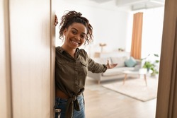 Welcome To My Home. Joyful Millennial Black Lady Opening Door And Gesturing Inviting To Come In Standing Indoors, Smiling To Camera. Real Estate Owner. Hospitality Concept