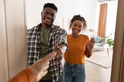 Hello. Cheerful Black Spouses Stretching Hands For Handshake Smiling To Camera Meeting Somebody Standing Near Opened Door At Home. Nice To Meet You, Welcome To Our House Concept. Selective Focus
