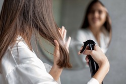 Haircare. Young Female Applying Hair Spray While Standing Near Mirror In Bathroom, Unrecognizable Millennial Woman Testing New Hairstyle Product At Home, Selective Focus On Her Reflection