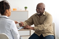 Medicine And Health Care Concept. Black female doctor giving elderly male patient pills, man holding tablets. Young specialist prescribing treatment to mature adult taking painkiller or vitamins