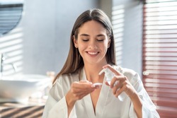Happy young lady applying hydrophilic oil on cotton pad for cleansing face, smiling beautiful woman making daily skincare routine in bathroom, enjoying making beauty treatments at home, free space