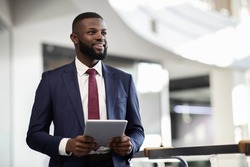 Cheerful young bearded african american man manager walking by office building corridor, holding modern digital tablet, using mobile app for business, looking at copy space and smiling, panorama