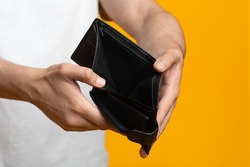 Financial crisis and bankruptcy while COVID-19 pandemic concept. Unrecognizable man showing empty wallet at camera, short of money, yellow studio background, copy space, cropped shot