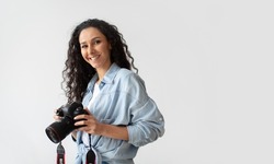 Professional Photographer Woman Holding Photo Camera Posing Smiling To Camera Standing Over White Wall Background. Lady Taking Photos Posing With Photocamera. Photography. Free Space For Text