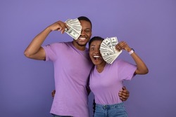 Joyful black man and woman won lottery, hugging and covering eye with bunch of money banknotes. Emotional lucky couple holding cash on purple violet studio background wall. Gambling, Loan Concept