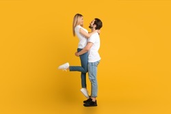 Cheerful young european male with beard raises female, isolated on yellow background, studio, full length, profile. Relationship, love, romance, advertising and offer, win and huge sale, copy space