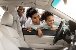 Cheerful Black Family Of Three Buying New Car, Looking Through Window At Auto Interior Choosing Luxury Automobile In Dealership. Vehicle Rent And Purchase Concept