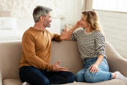 Cheerful Middle Aged Couple Talking And Flirting Enjoying Conversation Spending Time Together Sitting On Sofa At Home. Happy Marriage And Romantic Relationship Concept