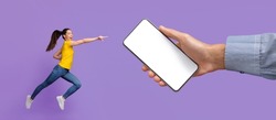 Mobile App Advert. Excited Cheerful Asian Woman Jumping Up And Pointing Finger At Huge White Empty Screen, Giant Hand Holding Big Cell Phone, Violet Purple Studio Wall. Check Gadget, Display Mock Up