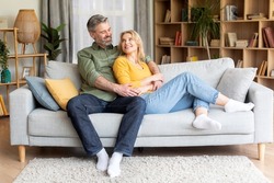 Romantic happy middle aged couple relaxing on couch at home, smiling loving mature spouses resting in cozy living room interior, embracing on sofa, enjoying weekend time together, copy space
