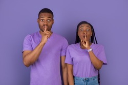 Shh, Keep Silence Concept. Emotional Black Couple Gesturing Hush Sign Posing Standing Isolated Over Purple Violet Studio Wall, Looking Staring At Camera. Holding Finger On Lips, Silent Gesture, Secret
