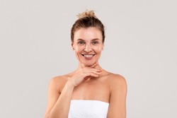 Mature Beauty. Portrait Of Attractive Middle Aged Woman Wrapped In Bath Towel Posing Over Light Grey Studio Background, Beautiful Female Touching Chin And Smiling At Camera, Copy Space