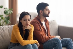 Marital Crisis. Unhappy Arabic Couple Sitting On Couch At Home, Having Relationship Problems. Bad Marriage, Breakup Concept. Selective Focus On Frustrated Woman