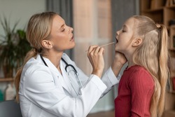 Angina, tonsillitis, cold and flu in children concept. Female doctor pediatrician checking patient little girl throat, child attending clinic, side view