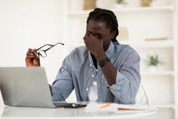 Male Freelancer Suffering Eyes Strain, Taking Off Glasses And Massaging Nose Bridge, Young African American Man Tired After Working On Laptop Computer At Home Office, Copy Space