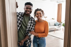 Welcome. Cheerful Black Couple Opening Entry Door Smiling To Camera Posing Standing At Home. Real Estate Buyers Meeting You In Modern Living Room Indoor. New House Ownership Concept