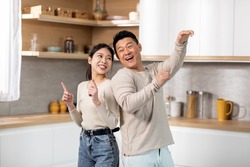 Crazy japanese couple having fun while cooking together at weekend at kitchen, positive asian middle aged man and young woman standing back to back, singing and dancing, copy space