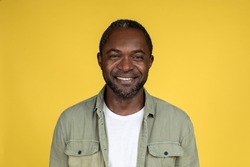 Headshot of smiling confident adult african american male in casual looking at camera, isolated on yellow background, studio, close up, free space. People emotions and facial expression, ad and offer