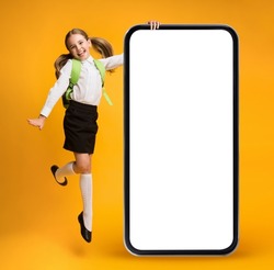 Excited Little Schoolgirl Jumping Near Huge Blank Smartphone With Empty White Screen, Positive Preteen Female Child Demonstrating Copy Space For Educational App Or Website Design, Collage, Mockup