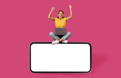 Cheerful excited surprised adult caucasian blonde lady with laptop raises hands, making victory, success gesture, sits on huge smartphone with blank screen, isolated on pink background. Ad and offer