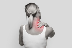 Neck pain muscle stress and strain concept. Stressed blonde woman massaging red sore neck, back view, black and white photo, studio background, copy space
