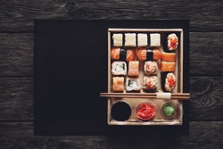Japanese food restaurant, sushi maki gunkan roll plate or platter set. ?opy space, chopsticks, ginger, soy sauce, wasabi. Sushi at rustic wood background in take away, delivery box. Top view. 