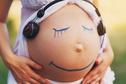 Pregnancy and music. Parenting and early development. Pregnant woman belly closeup with smiling funny face drawing, smiley symbol.