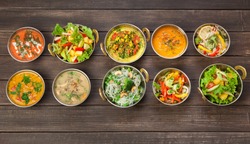 Vegan or vegetarian restaurant dishes top view, hot spicy indian soups, rice and salads in copper bowls. Traditional indian cuisine meal assortment on wood background. Healthy eastern local food