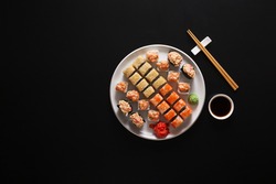 Japanese food restaurant, california salmon rolls, gunkans and sushi platter. Set with chopsticks and soy sauce. Top view on black background, vertical orientation with copy space
